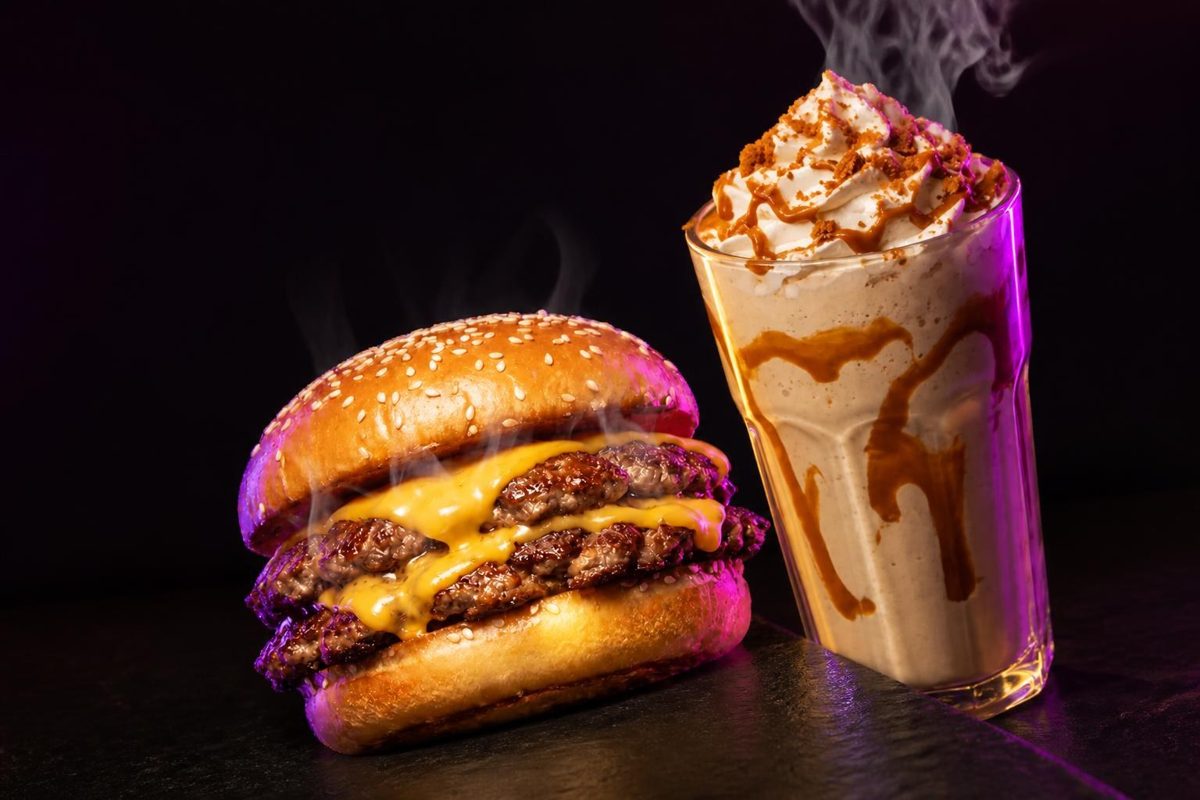 A So Famous Double Smashed burger beside a Biscoff milkshake on dark slate