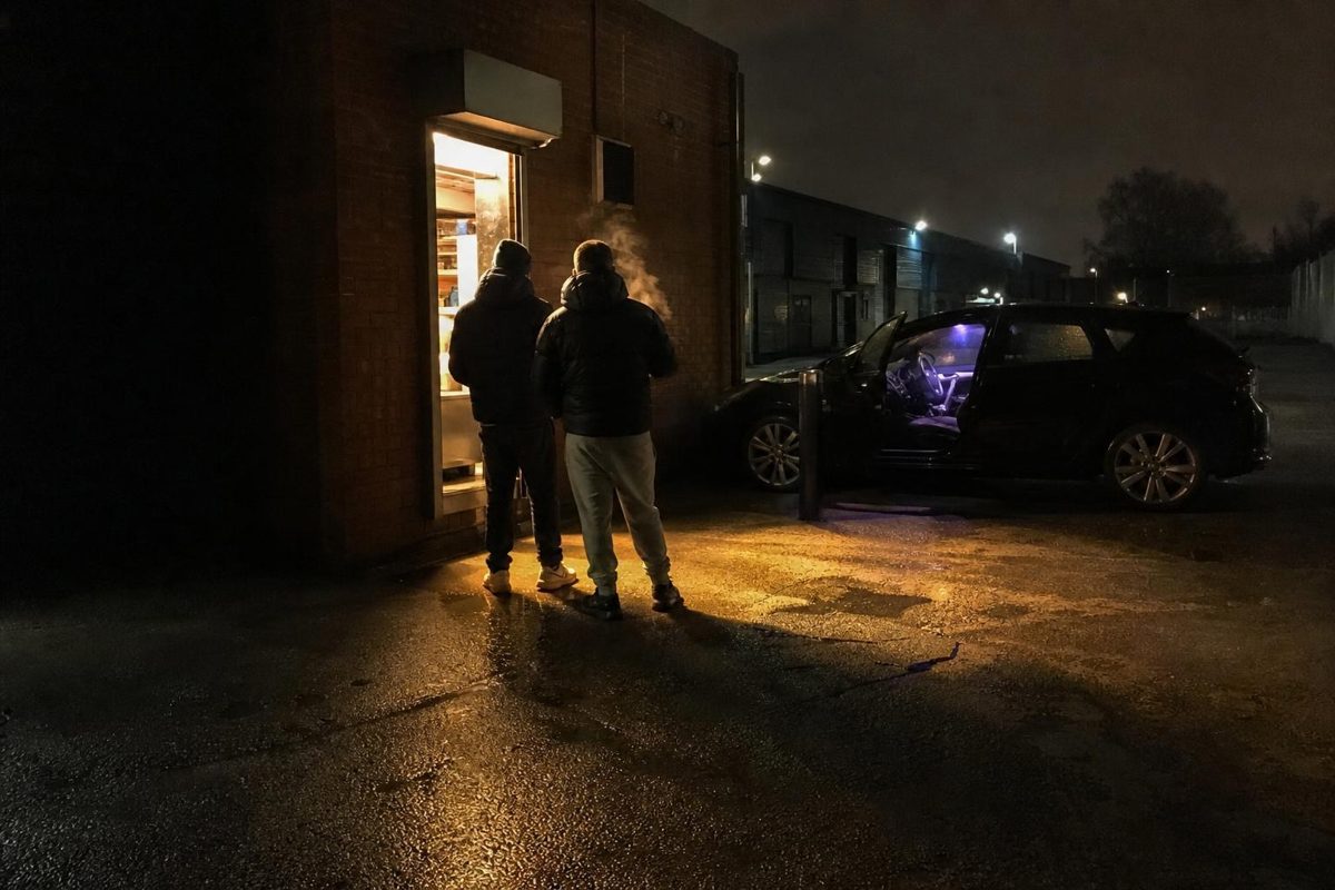 Two people collecting burger boxes from a takeaway doorway late at night in Manchester