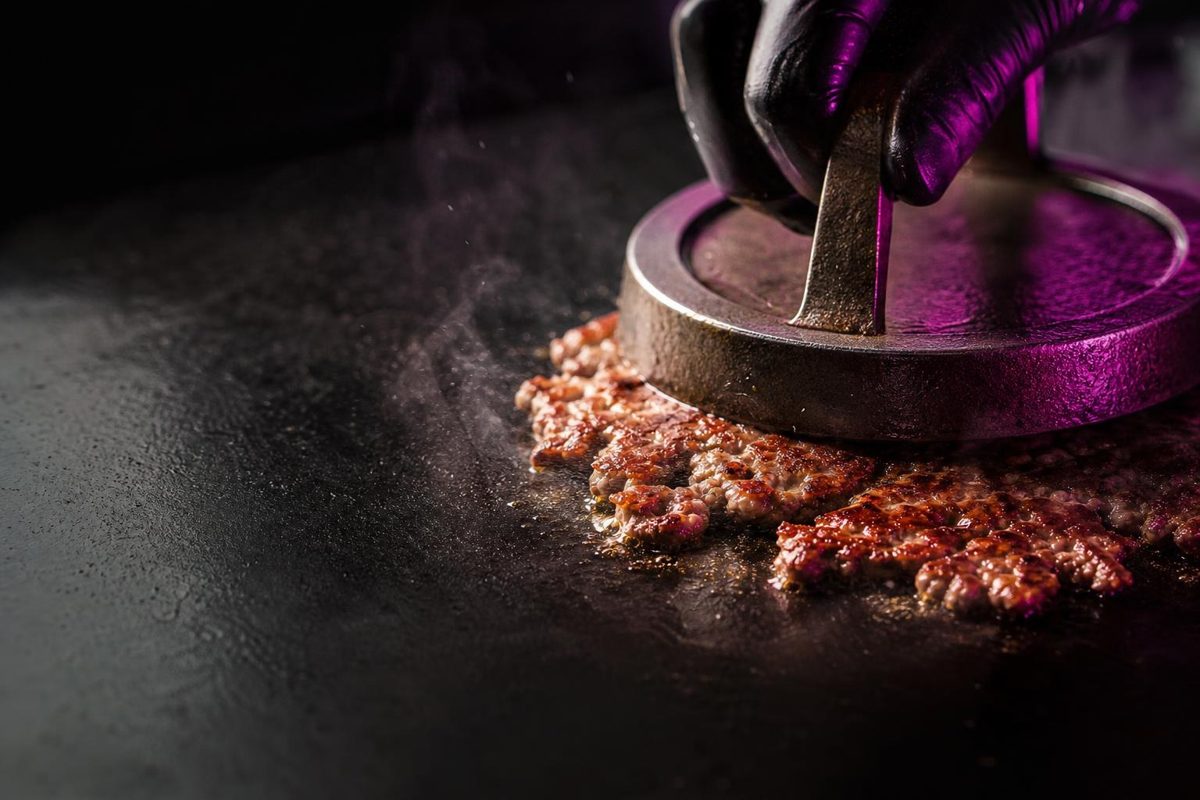 A beef patty being smashed on a hot flat-top grill, crisp edges forming